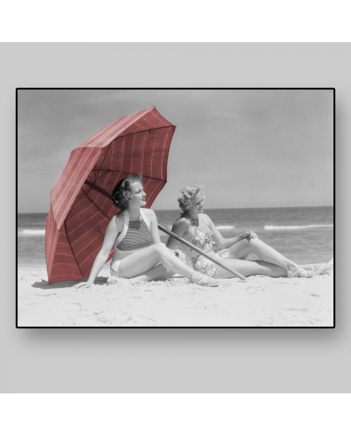 Two women sitting on beach under parasol,1930