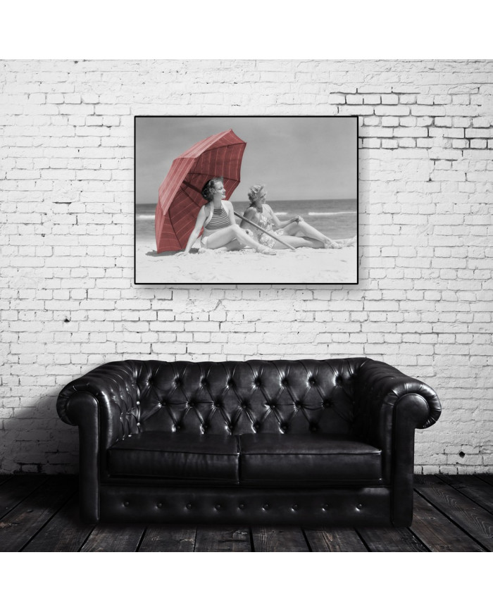 Two women sitting on beach under parasol,1930
