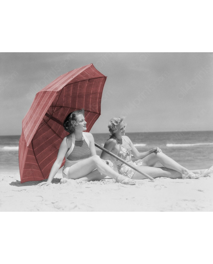 Two women sitting on beach under parasol,1930