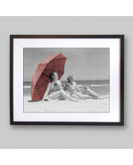 Two women sitting on beach under parasol,1930